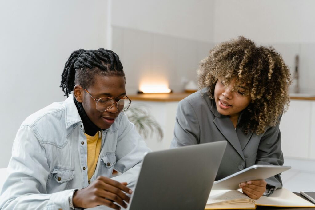 Two professionals discussing work on laptops and tablets in a modern office.