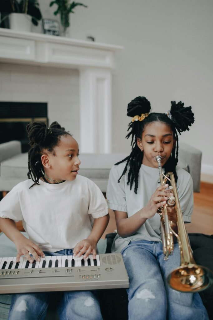 Two young girls playing keyboard and trumpet, enjoying music indoors.